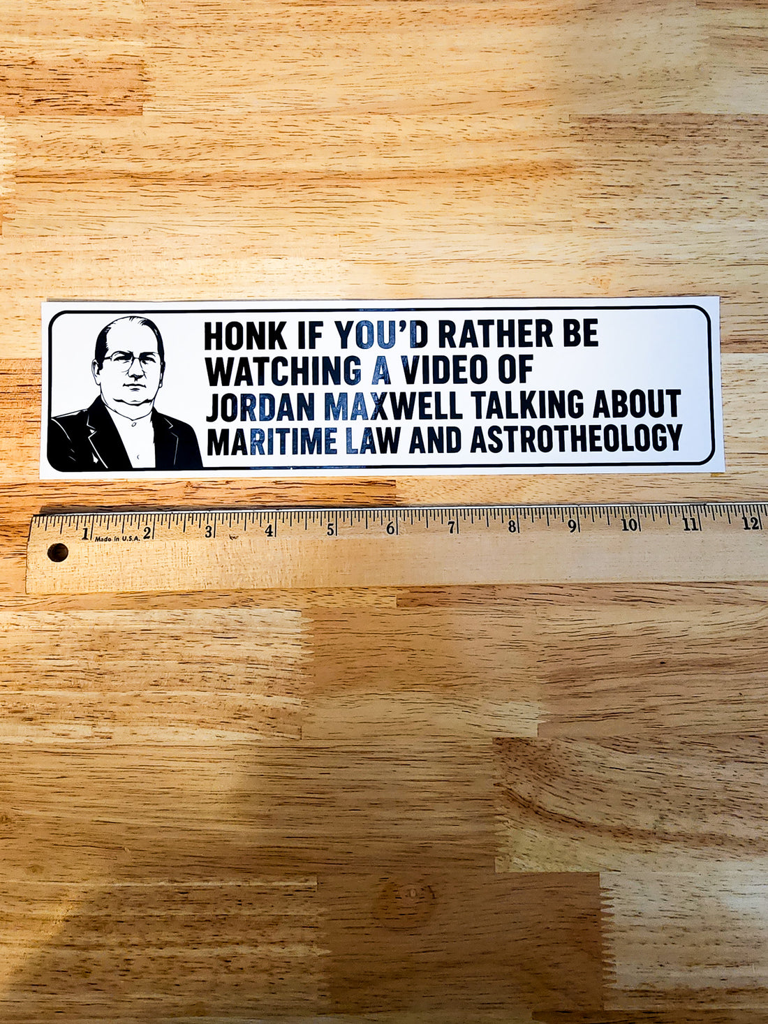 A rectangular bumper sticker with a black-and-white portrait of Jordan Maxwell and bold black text reading, &